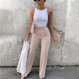 Woman wearing City Muse pants with a white top, showcasing high-waisted design and flared hem against a gray wall background.