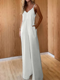 Woman wearing a Coastal Flow Jumpsuit with V-neckline and spaghetti straps, posing in wooden interior; ideal for beach or summer outings.