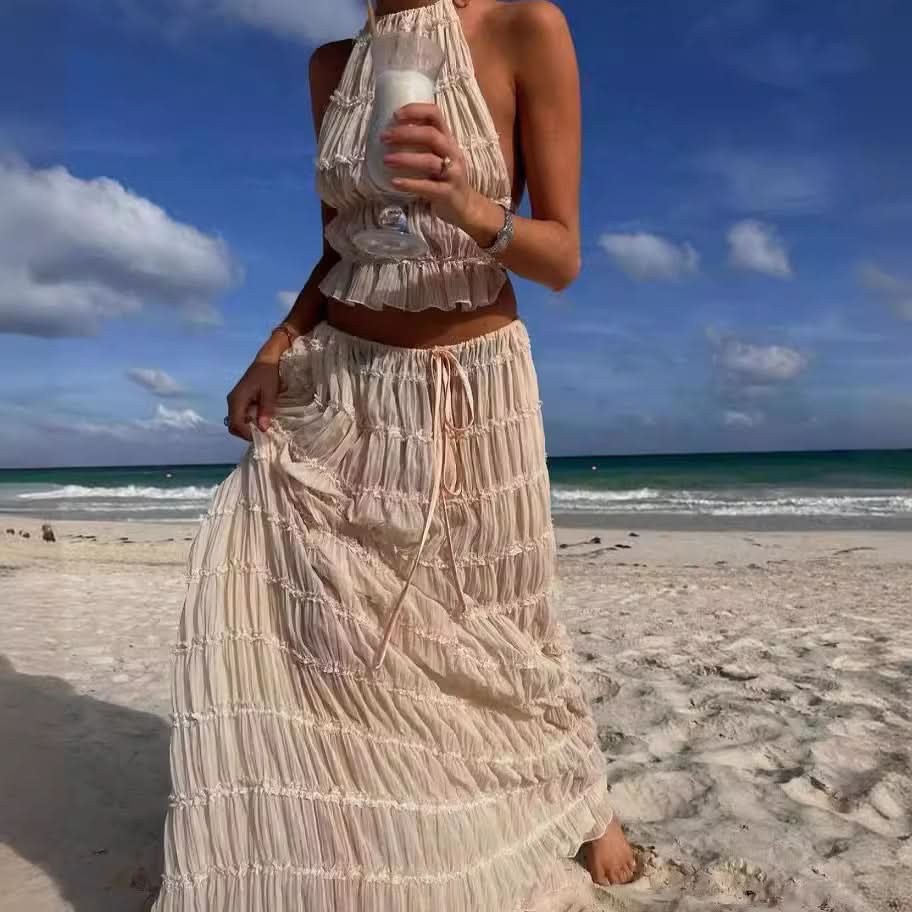 Woman wearing Isla Breeze Two-Piece Set, sleeveless crop top and flowy maxi skirt with crinkle fabric, on a sunny beach.