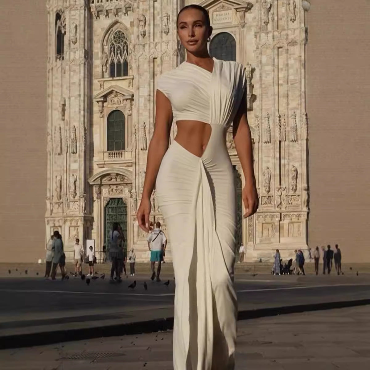 Woman in ivory white goddess draped cut-out gown walking in front of ornate historic building, exuding elegance and sophistication.