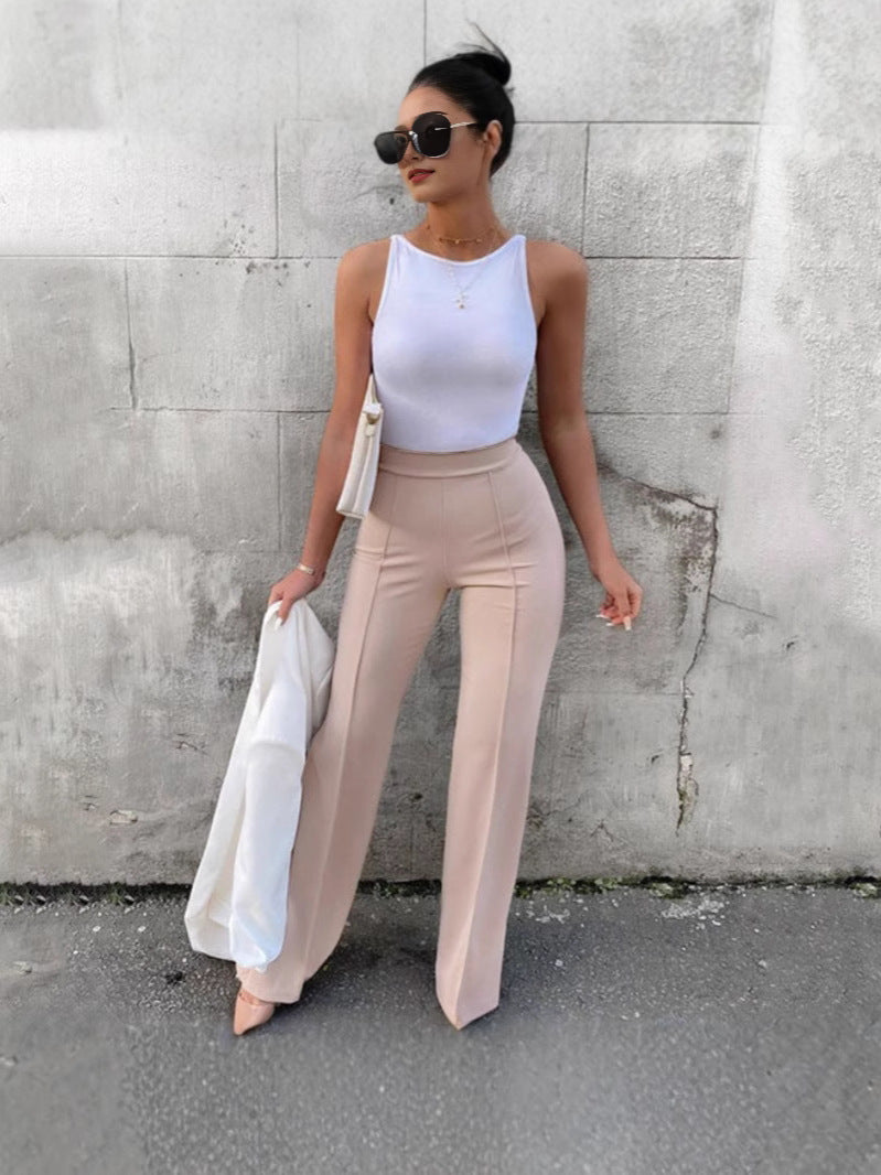 Woman wearing City Muse pants, sleek high-waisted trousers with flared hem styled with white top and sunglasses, holding a jacket.