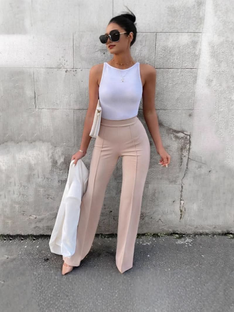 Woman wearing City Muse pants, sleek high-waisted trousers with flared hem styled with white top and sunglasses, holding a jacket.