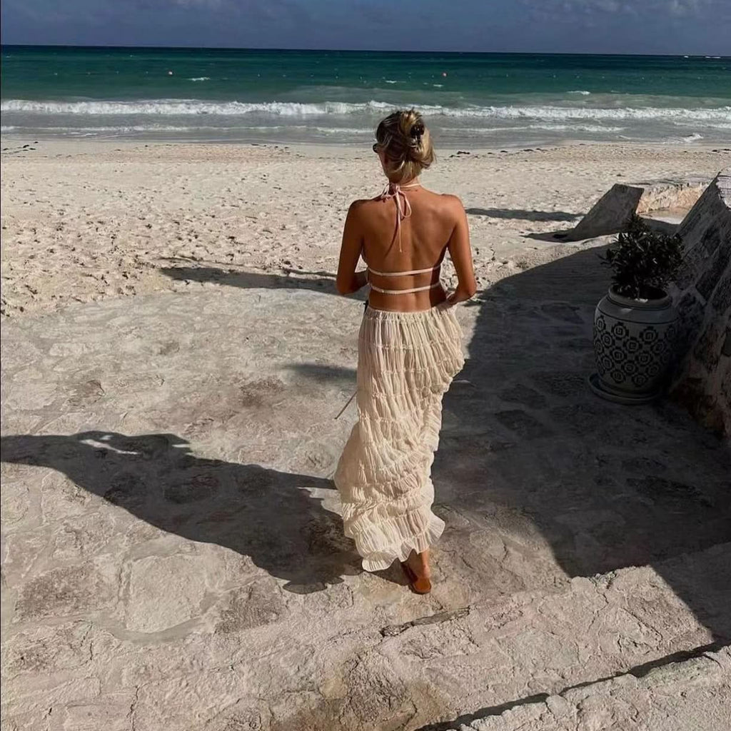 Woman in Isla Breeze Two-Piece Set walking on a sunny beach, featuring a high-neck, sleeveless crop top and flowy maxi skirt.