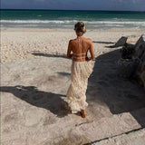 Woman in Isla Breeze Two-Piece Set walking on a sunny beach, featuring a high-neck, sleeveless crop top and flowy maxi skirt.
